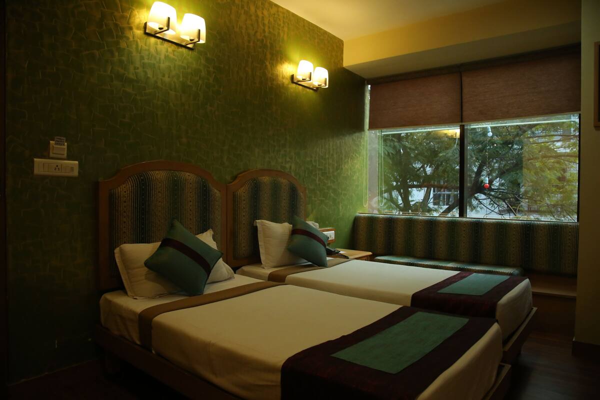 Habitación de hotel con dos camas, una ventana con vistas a árboles y luces fijadas a la pared.