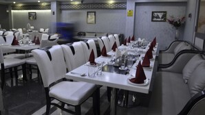 Un restaurante con sillas y mesas blancas, servilletas rojas y un florero con flores.
