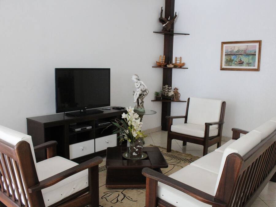 Una sala de estar con televisor, muebles de madera, un jarrón con flores y un cuadro en la pared.