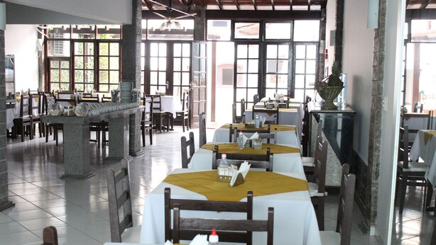 Un restaurante con varias mesas y sillas, amplias ventanas y piso de baldosas.