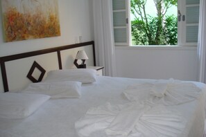 A hotel room with a neatly made bed, a bedside table with a lamp, and a window with shutters. - Hotel Pousada da Néia (Cananeia)