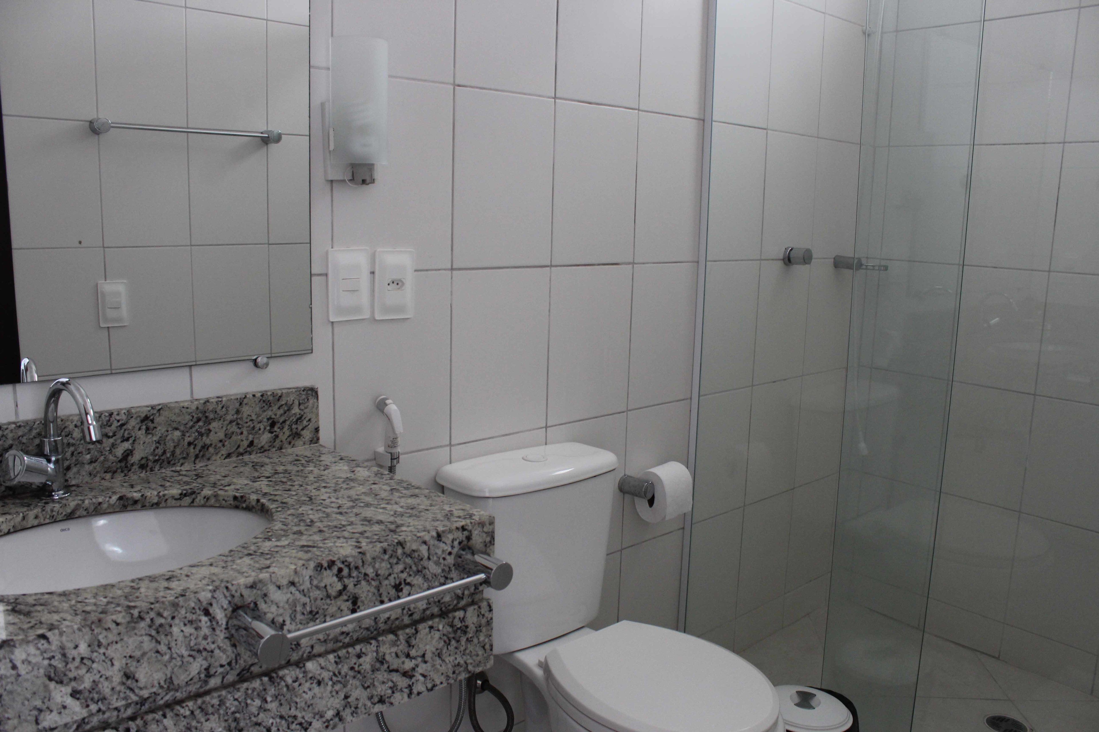 A bathroom with a granite sink, white toilet, and a glass shower enclosure.