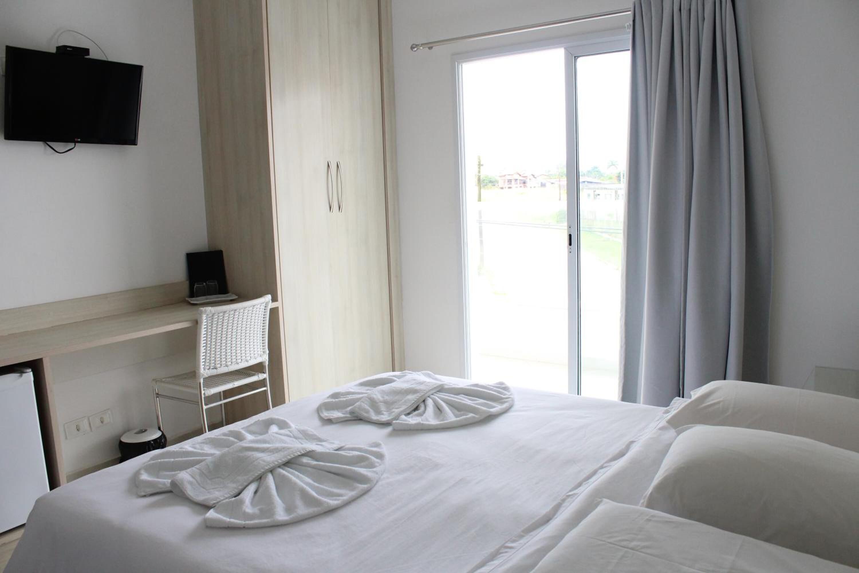 Ein Hotelzimmer mit einem Bett, einem Fernseher, einem Schreibtisch mit Computer sowie einer Glastür zum Außenbereich.