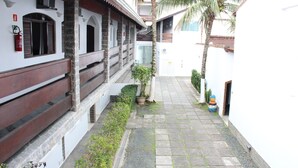 Un patio con un sendero de piedra, una palmera y un edificio de fachada blanca y vigas de madera.