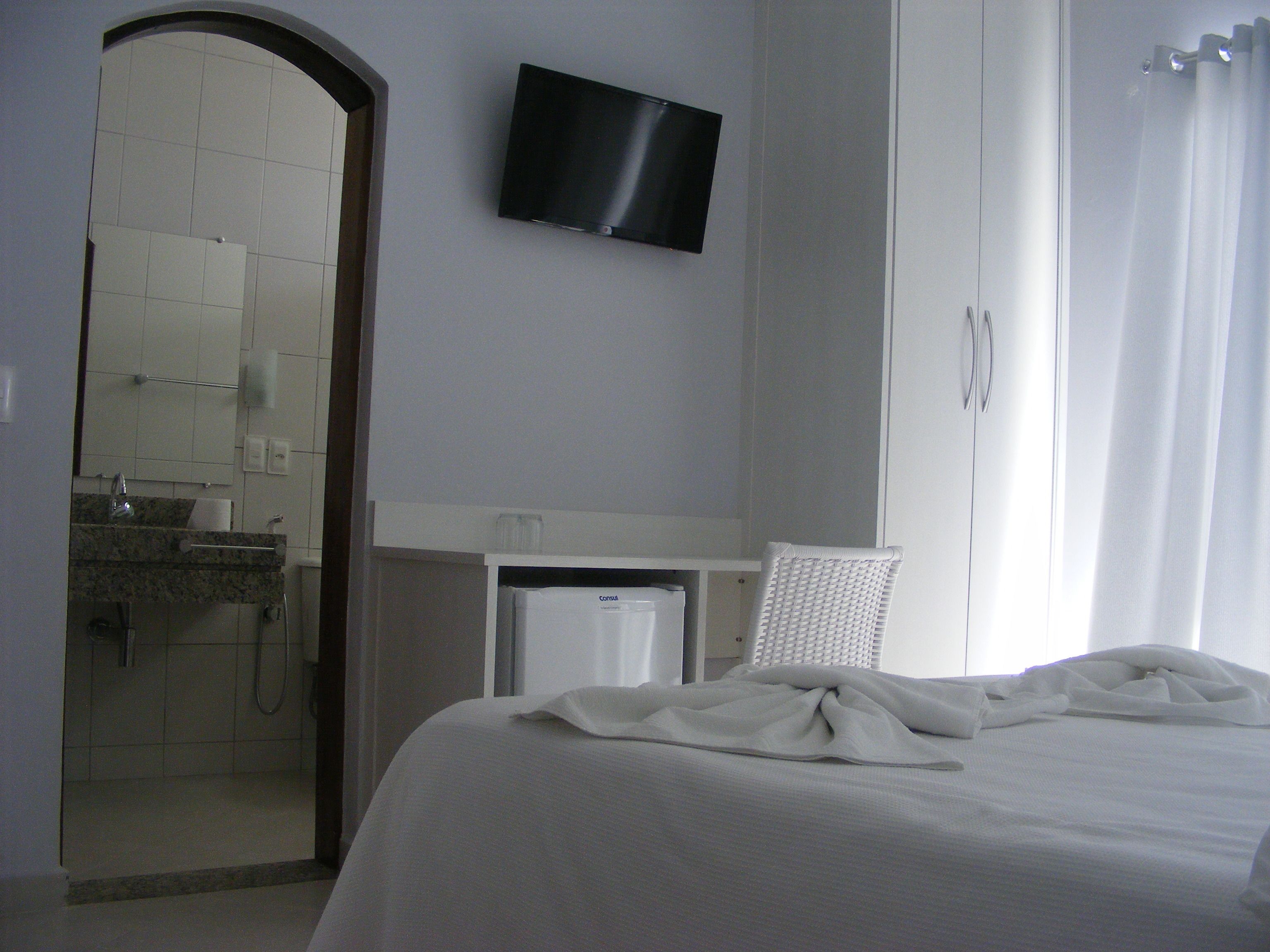 Habitación de hotel con cama, televisión montada en la pared, baño con ducha y escritorio con silla.