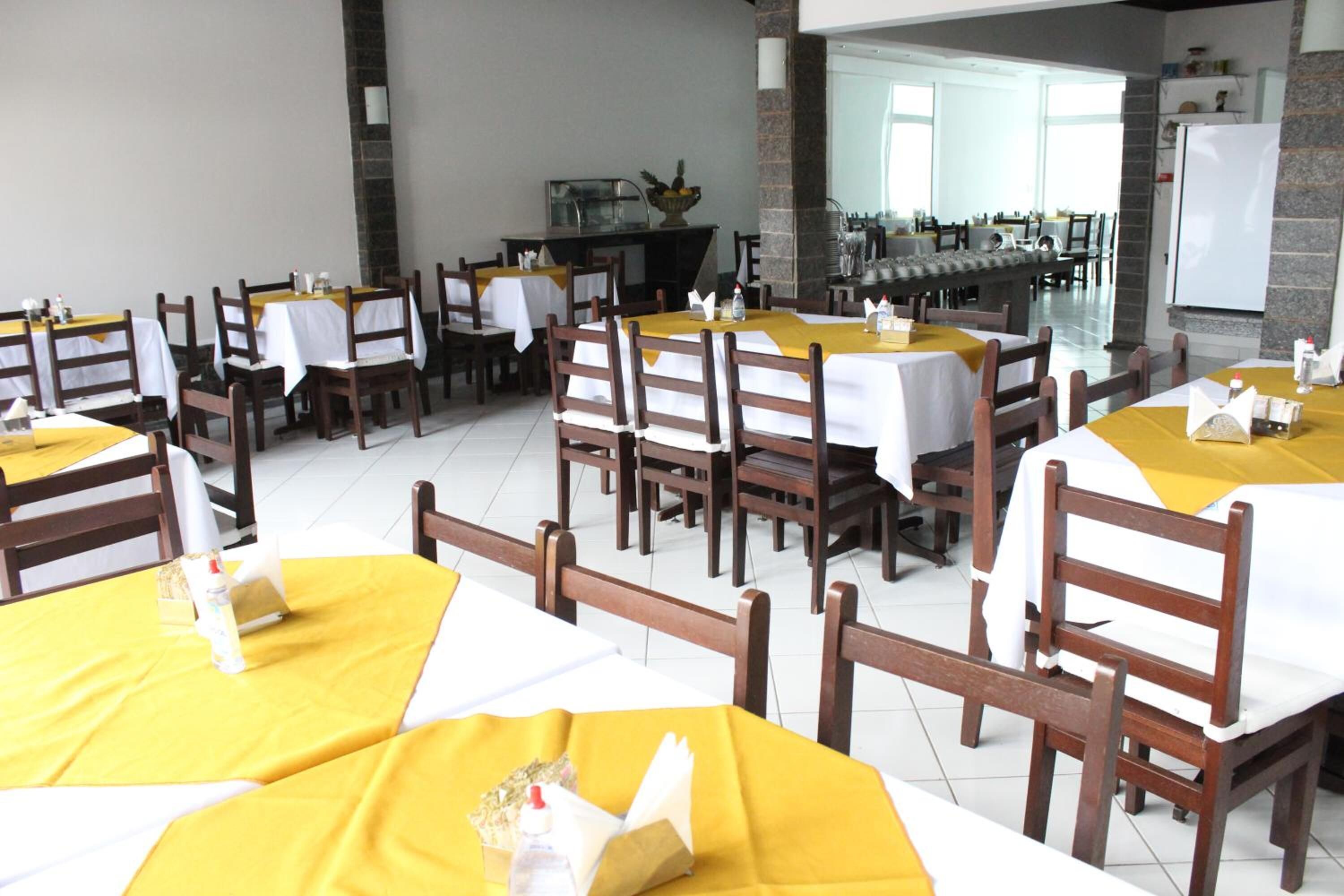 Comedor con mesas dispuestas para varios comensales, sillas de madera y un mostrador de buffet al fondo.