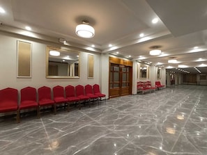 A spacious hall with rows of red chairs, a polished marble floor, and a wooden door with glass panels. - Hotel Avisha (Barasat)