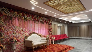 A stage with a white sofa and red chairs, a floral backdrop, and a patterned carpet. - Hotel Avisha (Barasat)