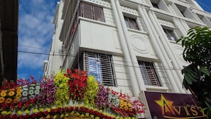 A hotel with a white facade, multiple balconies, and a flower display at the entrance. - Hotel Avisha (Barasat)