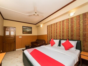 A hotel room with a bed, a chair, a desk, a ceiling fan, and a patterned wallpaper.