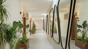A hallway with a long corridor, potted plants, and mirrors on the walls.