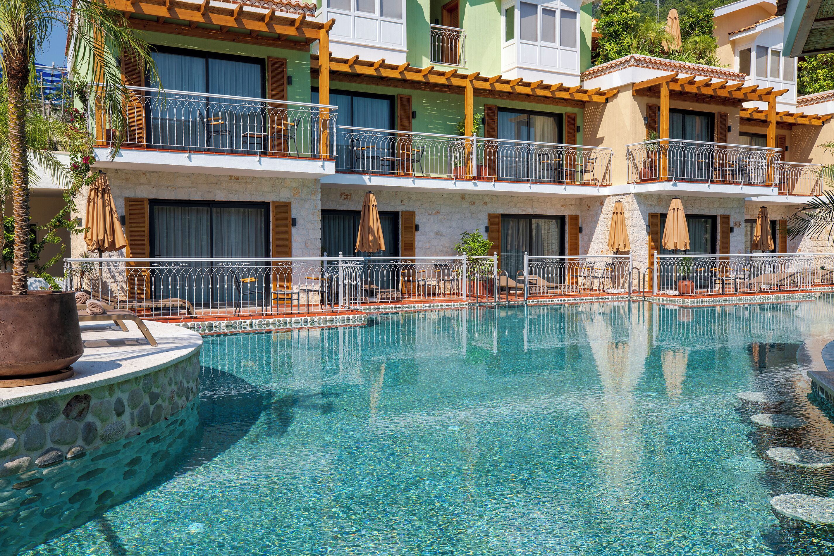 A hotel with a swimming pool, balconies with outdoor furniture, and potted plants.