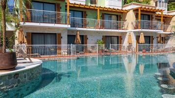 A hotel with a swimming pool, balconies with outdoor furniture, and potted plants.