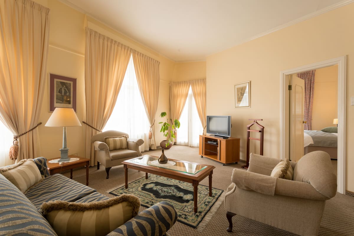 Une chambre d’hôtel avec un canapé, un fauteuil, une petite table avec une lampe, une télévision et une plante.