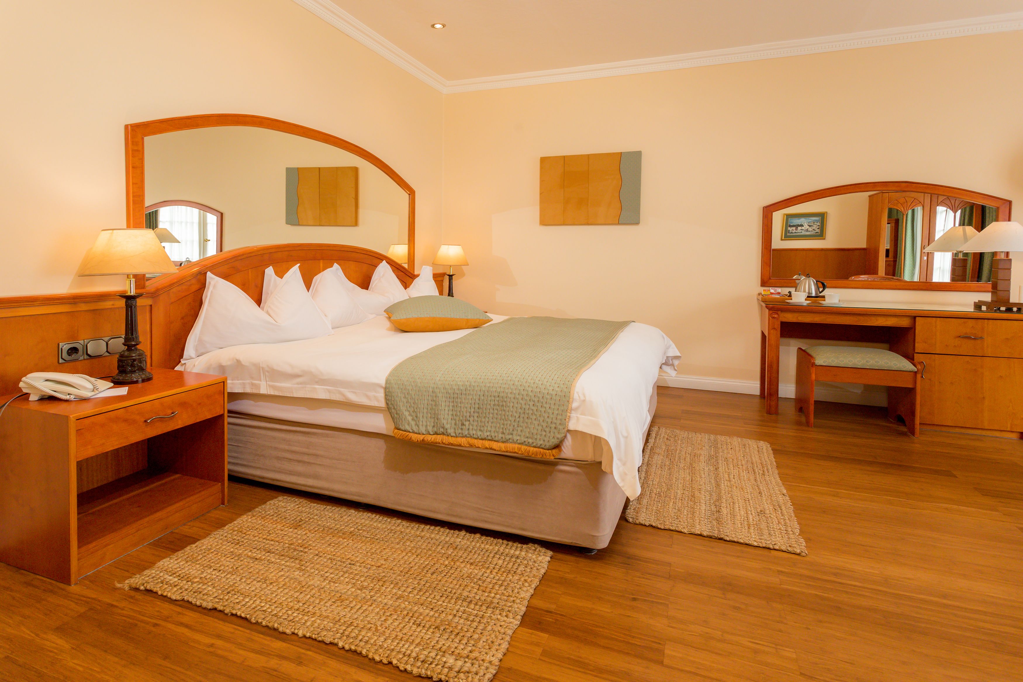 A hotel room with a bed, bedside tables, a desk, a chair, a desk lamp, a telephone, and a mirror.