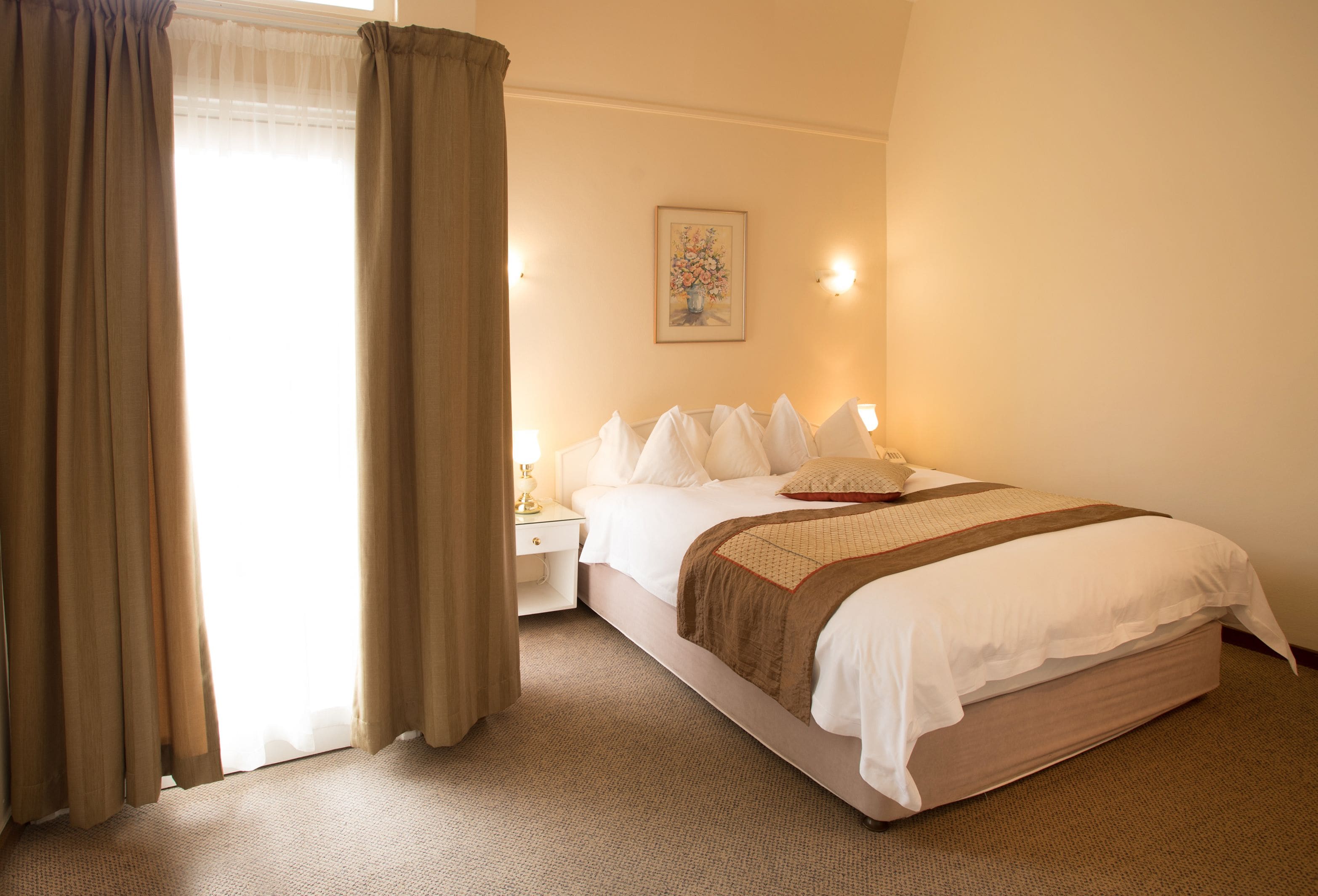 A hotel room with a bed, a nightstand, a lamp, and a painting on the wall.