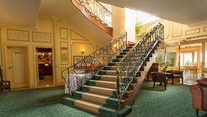 A grand staircase with ornate metal railings, carpeted steps, and a wooden finish. - Hansa Hotel (Swakopmund)