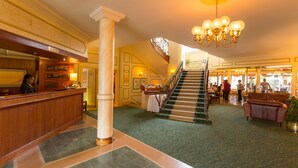 A hotel lobby with a reception desk, a staircase, and a seating area. - Hansa Hotel (Swakopmund)