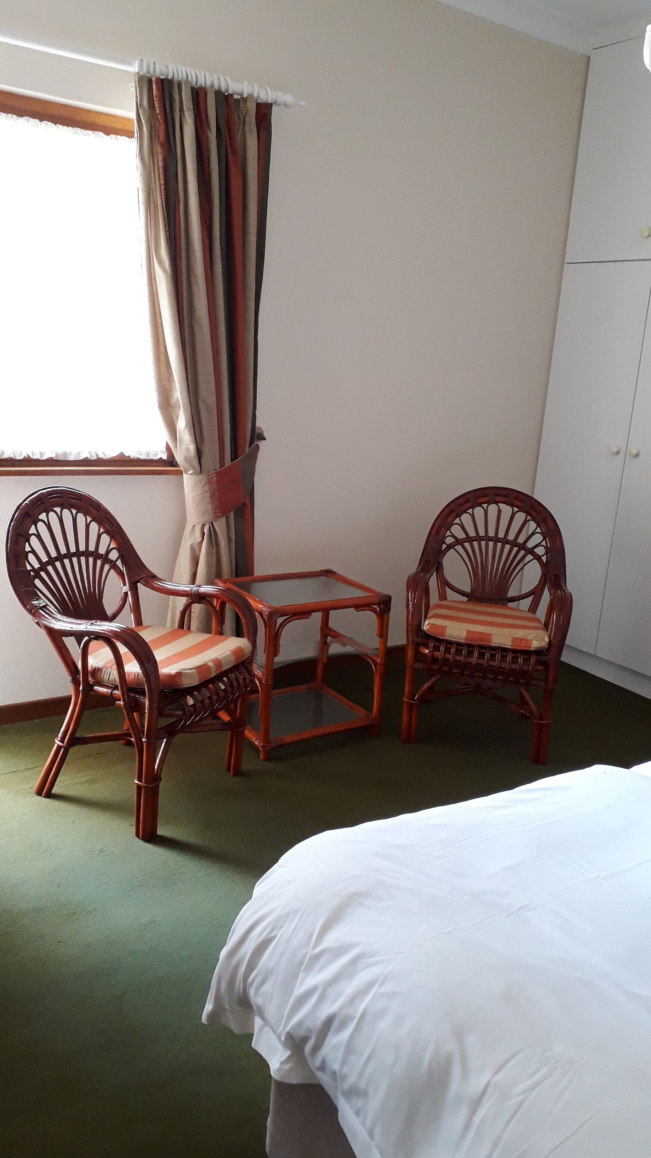 A room with a bed, two wicker chairs, a small table, and a window with curtains.