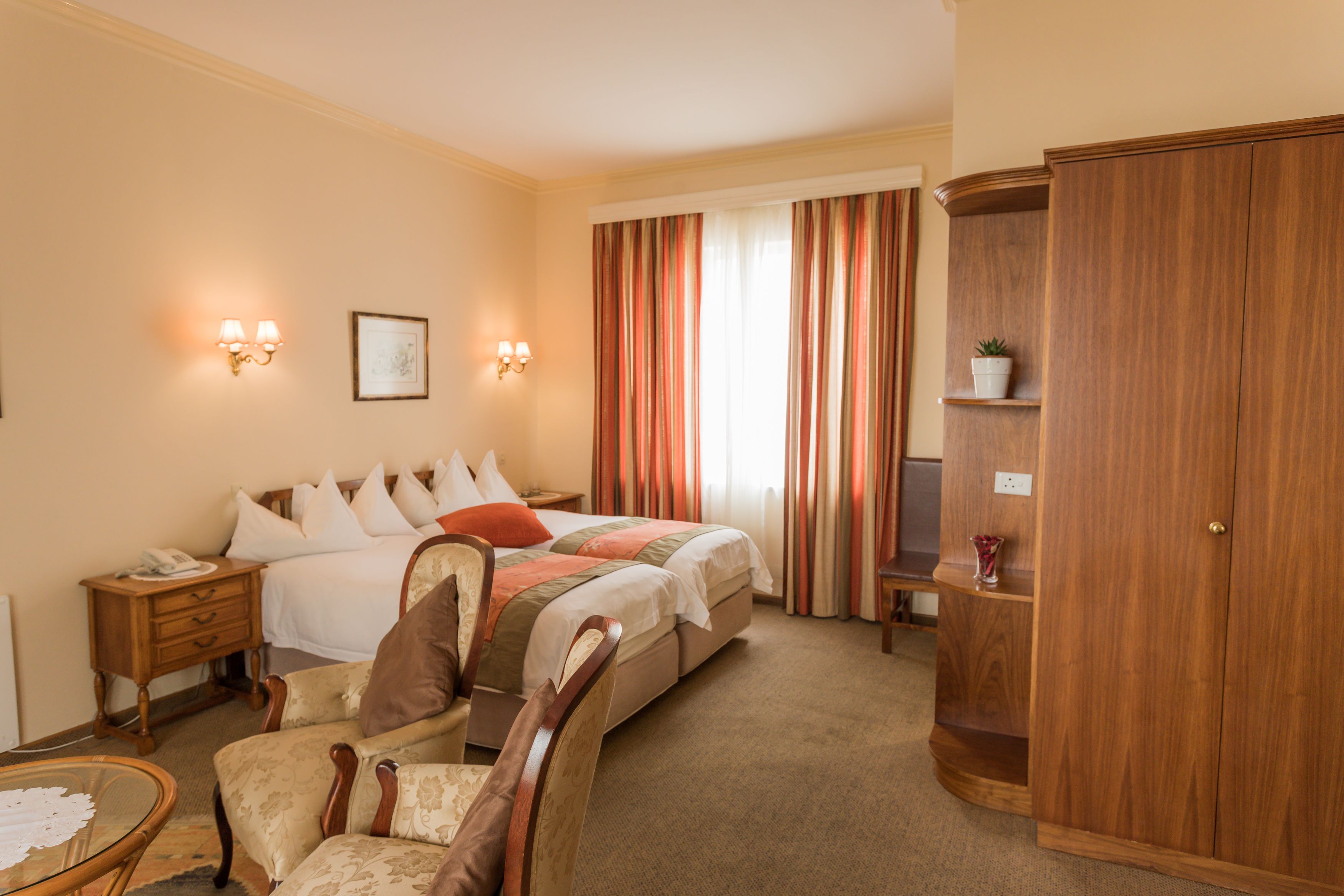 Habitación de hotel con cama, mesitas de noche, una silla, armario y ventana con cortinas.