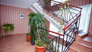 A staircase with a metal railing, surrounded by potted plants and a striped wallpapered wall. - City Hotel Tien Shan (Almaty)