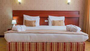 A large bed with a wooden headboard, white bedding, and two bedside lamps. - City Hotel Tien Shan (Almaty)