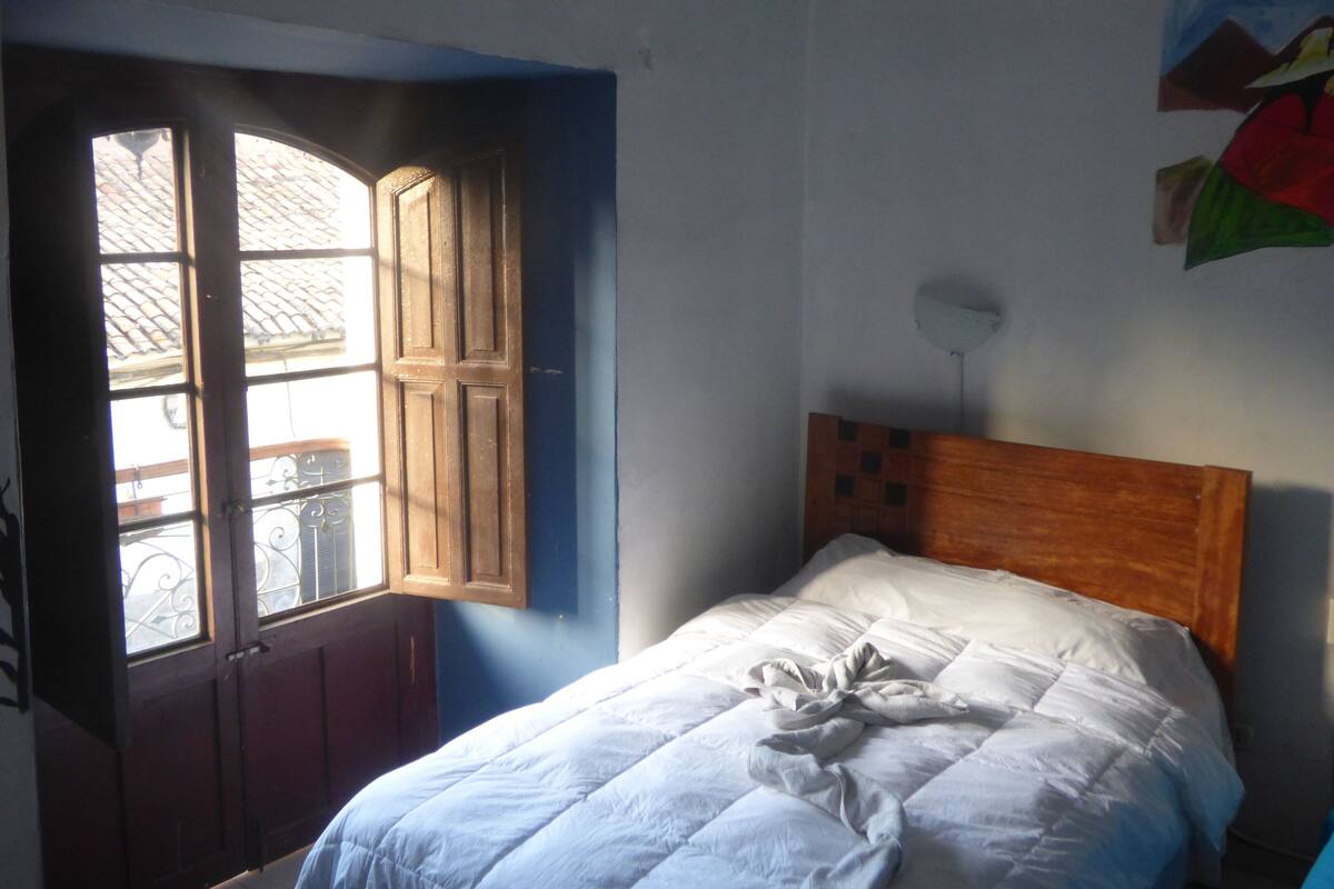 A bedroom with a wooden headboard, a bed with white bedding, and a window with a view of the outside.