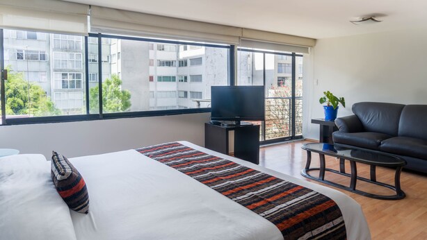 A modern hotel room with a large bed, a television, a sofa, and a balcony with a view of the city. - Grupo Kings Suites Platon 436 (Mexico City)
