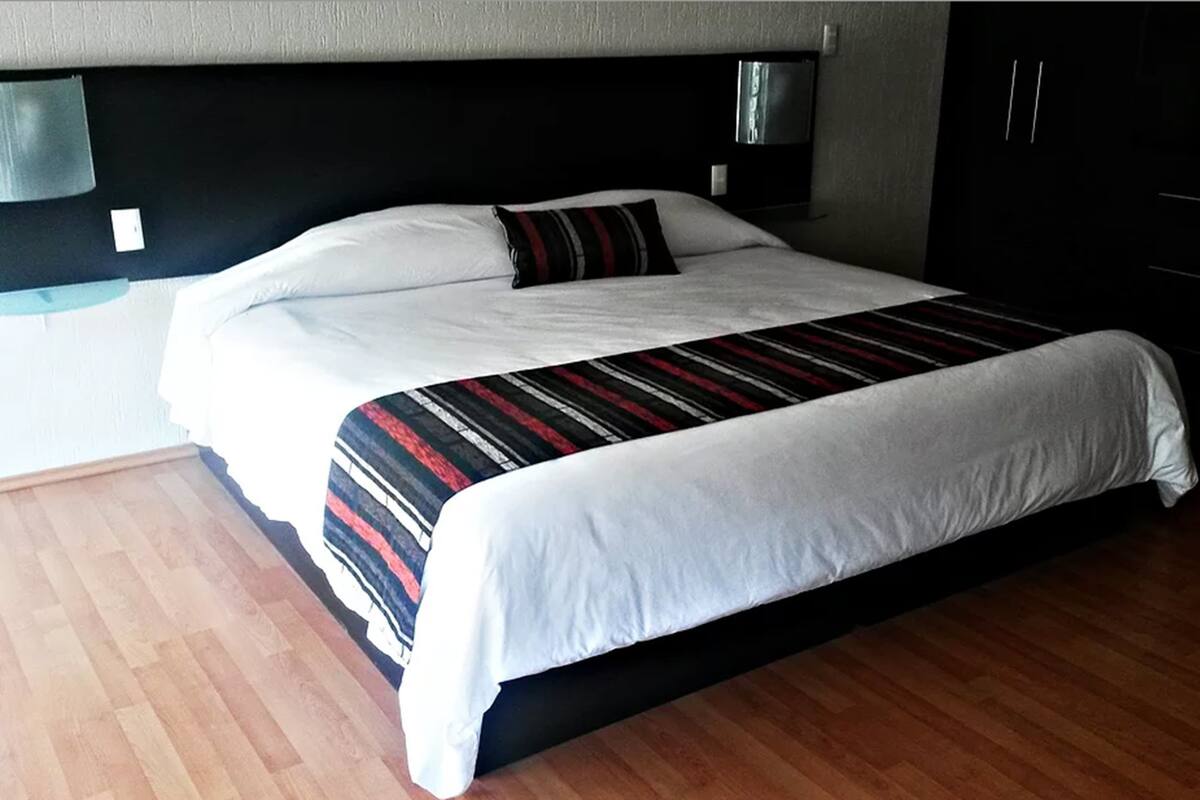 Una cama grande con un edredón a rayas, un cabecero negro y suelo de madera.