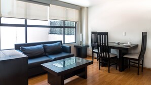 A modern living room with a sofa, a coffee table, a dining table with chairs, and large windows with blinds. - Grupo Kings Suites Platon 436 (Mexico City)
