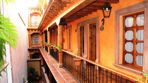 A narrow courtyard with a tiled floor, wooden balcony railings, and potted plants. - Hotel Refugio del Angel (Patzcuaro)
