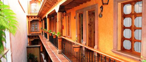 A narrow courtyard with a tiled floor, wooden balcony railings, and potted plants.