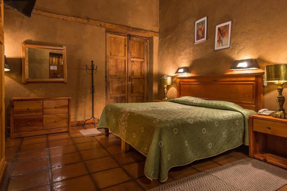 A bedroom with a bed, wooden wardrobe, a mirror, and two wall-mounted lamps.