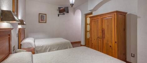 Quarto com duas camas, um guarda-roupa de madeira, uma televisão e um candelabro.