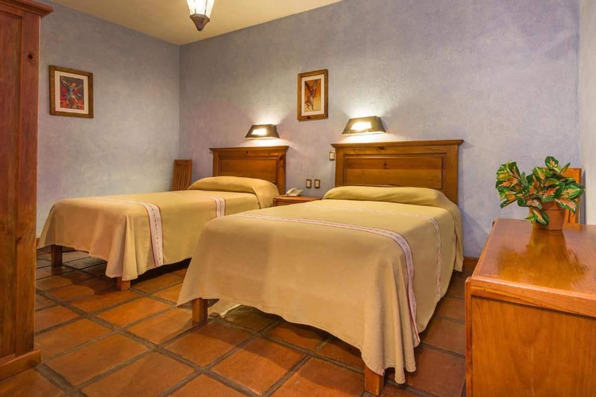 A hotel room with two beds, wooden headboards, and a small table with a plant.