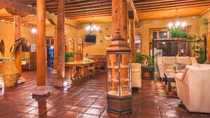 A spacious lobby with wooden beams, a tiled floor, a central seating area with a table and chairs, and a decorative glass display case. - Hotel Refugio del Angel (Patzcuaro)