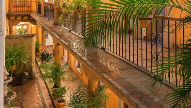 A courtyard with a wooden balcony, potted plants, and a tiled floor. - Hotel Refugio del Angel (Patzcuaro)