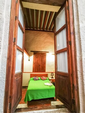 A narrow doorway leading to a room with a bed, a wooden wardrobe, and a small table with a lamp. - Hotel Del Callejon (Morelia)