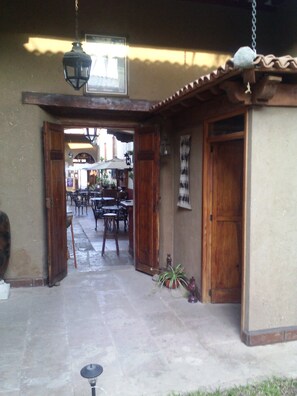 An outdoor patio area with wooden tables and chairs, a hanging lantern, and a door leading to the interior. - Hotel Del Callejon (Morelia)