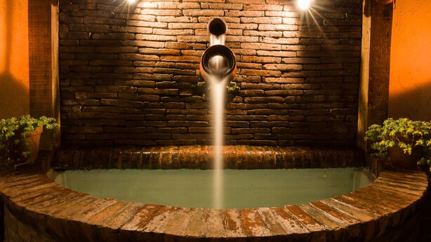 A circular hot tub with a brick wall backdrop and two spotlights. - Hotel Del Callejon (Morelia)