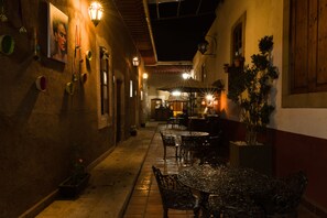 An outdoor café with tables and chairs, a potted plant, and a wall-mounted light fixture. - Hotel Del Callejon (Morelia)