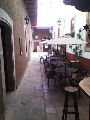 An outdoor café with tables and chairs, a tiled floor, and hanging lanterns. - Hotel Del Callejon (Morelia)