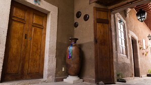 A rustic building with wooden doors and a large vase on a pedestal. - Hotel Del Callejon (Morelia)