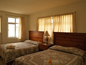 A hotel room with two beds, a nightstand, a lamp, and a window with curtains. - Hotel & Posada Refugio Independencia (Morelia)