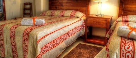 Habitación de hotel con dos camas, cabecero de madera, mesita de noche con lámpara y alfombra marrón.