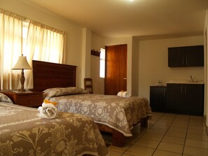 A hotel room with two beds, a nightstand with a lamp, a wooden wardrobe, and a small bathroom with a sink. - Hotel & Posada Refugio Independencia (Morelia)