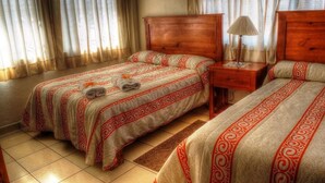 A hotel room with two beds, a wooden headboard, a nightstand with a lamp, and a window with curtains. - Hotel & Posada Refugio Independencia (Morelia)
