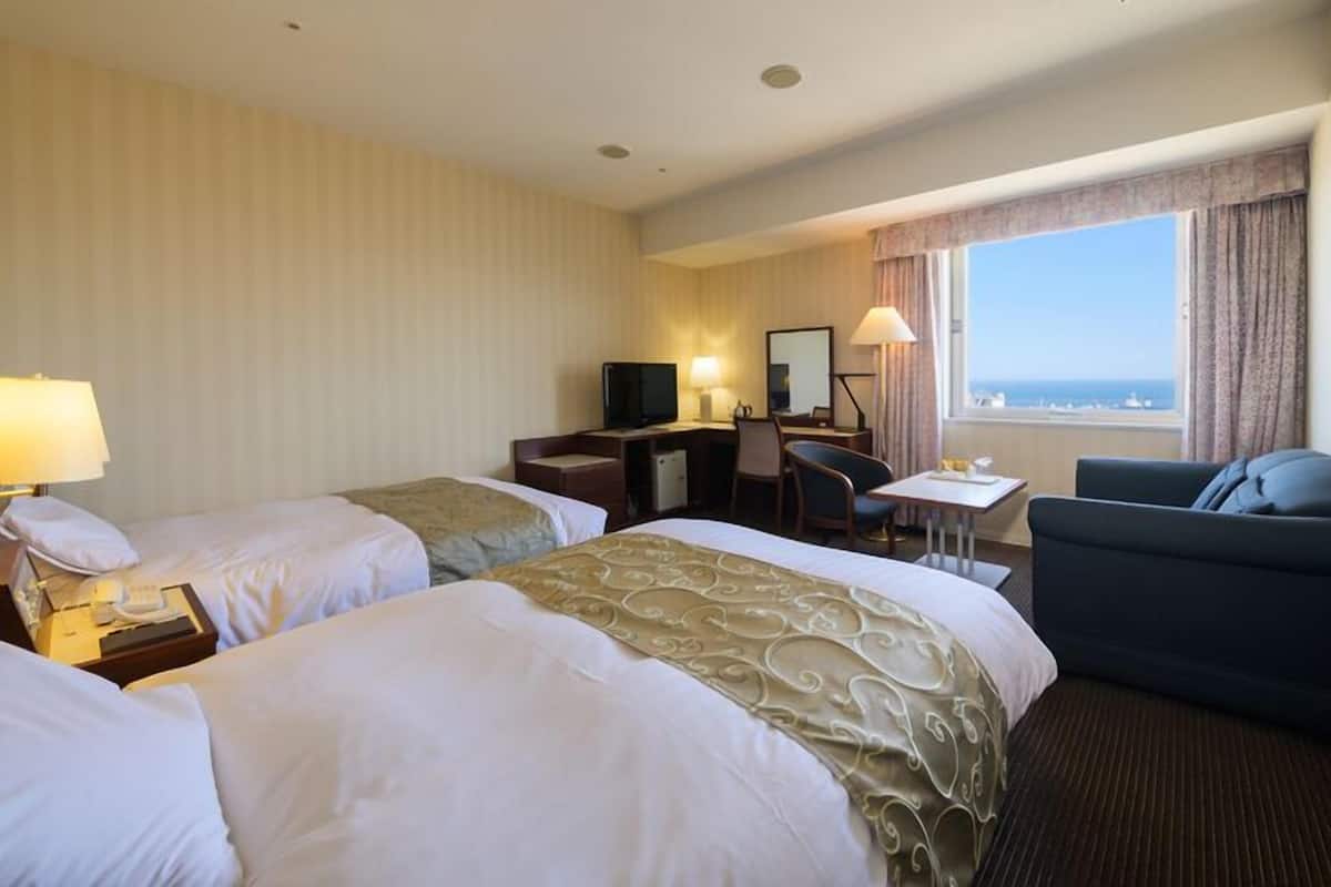 Une chambre d’hôtel avec deux lits, un bureau avec un ordinateur, une chaise, une petite table et une vue sur l’océan.