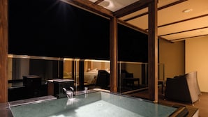 Una habitación de hotel moderna con un balcón acristalado, una cama grande y un baño con ducha acristalada.