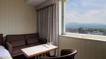 A hotel room with a sofa, a small table, and a view of a cityscape through a window.